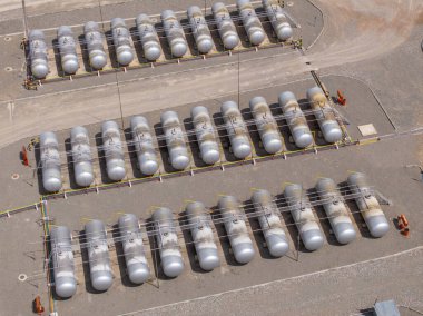 Endüstriyel bir ortamda, faydacı bir tasarım sergileyen sayısız depolama tankı var. Olay yeri, açık gökyüzünün altındaki kalabalık bir tesisin özünü yakalıyor..