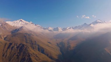 Güneşli bir günde Kırgızistan 'daki sonbahar dağlarının bulutlu ve karla kaplı tepelerinin havadan görüntüsü.