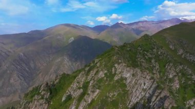 Kırgızistan 'ın engebeli dağ manzarasını gösteren hava aracı görüntüleri. Parçalı bulutlu gökyüzünün altındaki yeşil vadiler ve kayalık tepeler bölgenin doğal güzelliğini gözler önüne seriyor..