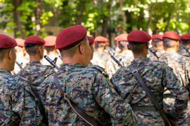 Genç tanınmayan Asyalı askerler kamuflaj üniformaları ve kırmızı bereliler ciddi bir şekilde yürüyorlar..