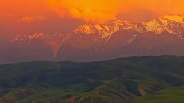 Kırgızistan 'daki yeşil eteklerin üzerinde görkemli karlı dağlar yükseliyor. Paraşüt efekti için aracın sağındaki kamera ile drone görüntüsü.