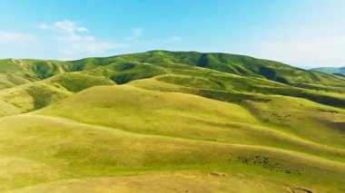 Kırgızistan 'da yaz gününde bulutlar seyrek, mavi gökyüzünün altında yuvarlanan yeşil tepeler, kameralı uzaktan kumandalı insansız hava aracı görüntüsü..
