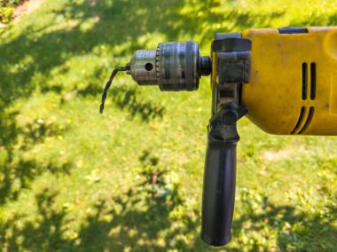 Man confidently holds a drill with bent cheap chinese drill bit in outdoor garden during daytime