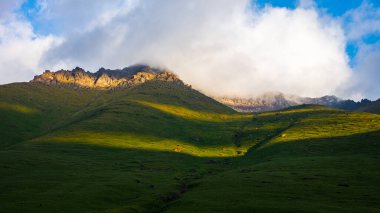 Huzurlu bir dağlık bölgede kayalık arazinin üzerinde görkemli dağlar yükselir. Gündüz güneşi manzarayı yıkıyor, doğada sakin bir atmosfer yaratıyor..