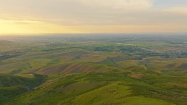 Kırgızistan 'ın geniş kırsal kesiminde uzak köyü olan açık bir gökyüzünün altında yuvarlanan yeşil tepeler yer alıyor. Drone görünümü.