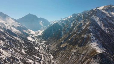 Hava manzarası, Kırgızistan 'da karla kaplı engin dağlar ve sakin bir dere yakalar. Kamyon doğru harekete.
