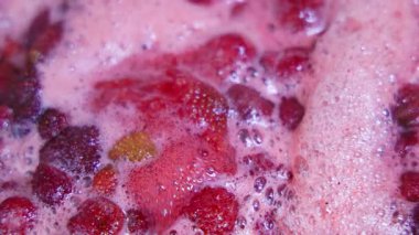 Sıcak bir mutfakta taze çilekler kaynıyor ve sıcak bir atmosfer yaratıyor. Lezzetli koku havayı dolduruyor. Tam kare makro görünüm