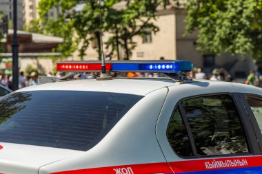 Kırgızistan polis arabasının aktif kırmızı ve mavi acil durum ışıkları güneşli yaz gününde işlek şehir caddesinde alarmda duruyor. Arka plandaki bulanık insanlar, Bişkek, Kırgızistan 'da 8 Mayıs 2025' te acil durum ve faaliyet hissi yaratıyorlar.