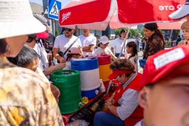 Kırgızistan 'ın Bişkek kentindeki canlı bir atmosferde susuz müşterilere içki servisi yapan, Şoro içecek arabası işleten kadınların etrafında toplanmış bir grup insan görülüyor - 8 Mayıs 2025