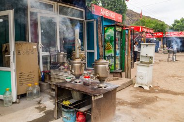 Semaverler yol kenarındaki kafede buhar püskürtürken kadınlar gözlerini kaçırıyor. Toprak ve dükkanlar Cholok, Kırgızistan 'da 16 Temmuz 2024' te sıcak ve kırsal bir atmosfer yaratıyor.