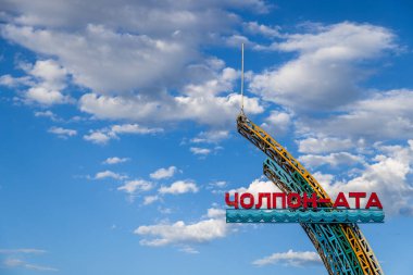 Kırgızistan 'daki Issyk-Kul Gölü' ndeki Cholpon-Ata kasabasına hoş geldin işareti. Büyük kırmızı harfler ve mavi dalgalı bir kenar var. Bulutları dağılmış, açık mavi bir gökyüzüne karşı, iyimserlik yayıyor..