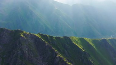 Berrak gökyüzünün altındaki görkemli dağların sakin manzarası. Yeşil yamaçlar ve sis barışçıl atmosfere ekleniyor, doğa severler için mükemmel. Drone görünümü.