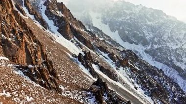 Stark ve ıssız arazi görkemli karla kaplı dağları gösteriyor. Engebeli kayalık yamaçlar açık mavi gökyüzü altında soğuk, nefes kesici bir manzara yaratır..