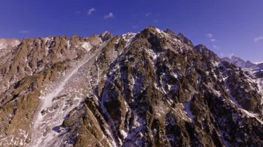 Uçsuz bucaksız vadideki kayalık arazide karlı dağ tepeleri kulesi. Kamyon ile drone görüntüsü sağ kamera hareketi.