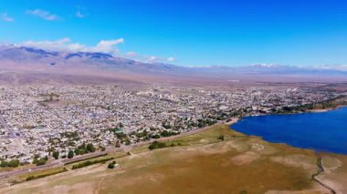 Serin Issyk-Kul Gölü ve Kırgızistan 'daki görkemli dağların yanına kurulmuş büyüleyici Balykchy şehir manzarası havadan görülüyor. Parlak gündüz ışığı doğal güzelliği artırır..
