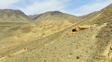 Sersemletici dağ manzarası kaya oluşumları ve seyrek bitki örtüsüyle çöl arazisi içerir. Güneşli bir gökyüzünün altında çorak topraklar boyunca kirli bir yol esiyor..