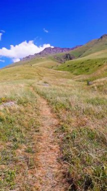 Asfaltsız yol, otlak yamaçtan kayalık dağ zirvesine doğru keşfe davet ediyor. Açık gökyüzü altındaki manzara sükunet ve macerayı çağrıştırıyor.