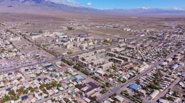 Hava görüntüsü, dağlarla çevrili yarı kurak arazide yer alan geniş Balykchy şehrini yakalar. Açık gökyüzü sessiz, panoramik sahneyi güçlendirir.