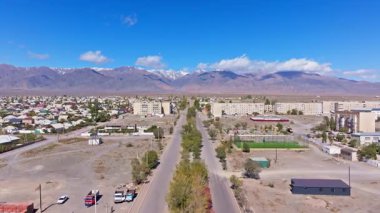 Hava manzarası, çok katlı binalar ve açık mavi gökyüzü altındaki ağaçlarla huzurlu yarı kurak Balykchy kasabasını yakalıyor. Manzaralı dağlar geniş bir zemin sağlar..