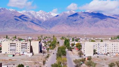 Hava manzarası, kasabanın yakınındaki arabalarla ve kamyonla sakin bir manzara yakalıyor. Karla kaplı dağlar gökyüzünün altında ihtişamlı bir şekilde yükselir..