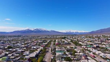 Kırgızistan 'da geniş dağlarla çevrili sakin küçük Balykchy kasabasını hava manzarası yakalar. Açık gökyüzü, gün içinde huzurlu kırsal manzarayı güzelleştirir.