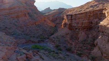Gökyüzü görüntüsü Kırgızistan 'da geniş kanyon ve eşsiz kaya oluşumlarını yakalar. Temiz bir gökyüzünün altında toprak yol ve sakin açık hava manzarası var..