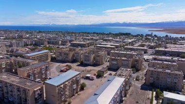 Issyk-Kul gölü yakınlarındaki modern binalar ve apartman bloklarının yer aldığı geniş Balykchy şehir manzarası. Dağlar parlak gün ışığında dingin bir zemin oluşturur..