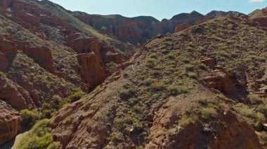 Hava görüntüsü Kırgızistan 'daki geniş Konorchek çöl kanyonunu gösteriyor. Engebeli kaya oluşumları ve kuru toprak mavi gökyüzünün altında huzurlu doğal bir manzara yaratır..
