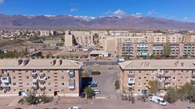 Yetişkin beyaz adam, belirsiz insanlar, araçlar ve inşaat ekipmanlarıyla çevrili şehir ortamında duruyor. Barışçıl gündüz sahnesinde arka planda dağlar var.