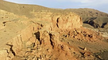 Geniş çöl manzarasında Kırgızistan 'da çarpıcı jeolojik oluşumlar ve kanyonlar bulunur. Dolly ileri kamera hareketi ile drone görüntüsü.