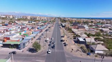 Birkaç araba açık gökyüzü altında işlek şehir yolunda ilerliyor. Binalar ve konteynırlar, Balykchy, Kırgızistan 'da uzak dağlar ve su manzaralı cadde boyunca dizili. 2 Ekim 2025