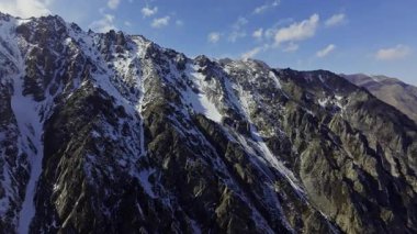 Geniş dağ siluetleri karla kaplı engebeli zirveler. Dolly ileri kamera hareketi ile drone görüntüsü.