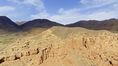 Kırgızistan 'ın Kokpak Kırgızistan çölündeki aşınmış kumtaşı dağlarını görüntüler. Görkemli kaya oluşumları, açık gündüz gökyüzü altında sahneye hakim..