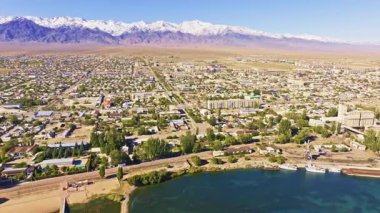 Serene Balykchy şehri sakin bir Issyk-Kul gölü boyunca binalar ve tekneler barındırır. Dağlar, açık mavi gökyüzünün altında görkemli bir şekilde yükselir..