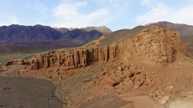 Uçsuz bucaksız çöl manzarası, berrak gökyüzüne karşı rüzgarla şekillendirilmiş kaya oluşumlarına sahiptir. Sakin atmosfer Kırgızistan dağlarının doğal güzelliğini vurguluyor.