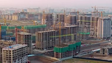 Kırgızistan, Bişkek 'te inşa edilen yüksek binaların insansız hava araçlarıyla çekilmiş görüntüleri. Belirsiz şehir manzarasının ortasında birden fazla beton yapı, kule vinçleri, yeşil güvenlik ağları ve kazı çalışmaları görülüyor.