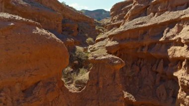Drone görüntüsü Kırgızistan çöl kanyonundaki sakin kumtaşı oluşumlarını yakalıyor. Kuru bitki örtüsü, berrak bir gökyüzünün altındaki görkemli manzarayı tamamlıyor..