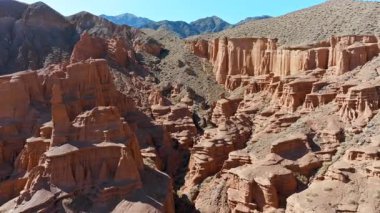 Geniş çöl kanyonu, berrak gökyüzünün altında kırmızı kaya oluşumlarını sergiliyor. Uçan dron görüntüsü ileri.