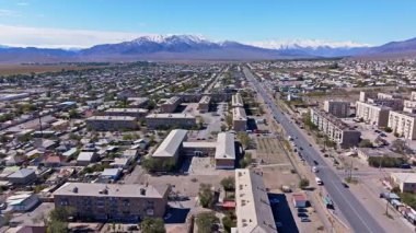 Geniş Balykchy kasabası, yerleşim binaları ve ana yolu ile havadan görülebiliyor. Arkaplanda karlı dağlar beliriyor berrak, güneşli bir gökyüzünün altında.