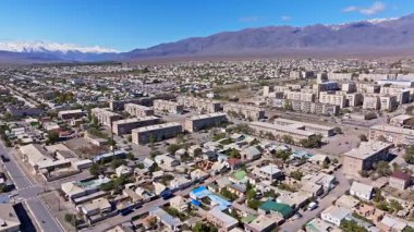Hava manzarası vadideki geniş şehir manzarasını yakalar. Yerleşim yerleri ve yollar açık gökyüzünün altındaki uzak karlı dağlarla tezat oluşturuyor..
