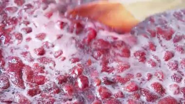 Sıcak bir mutfakta karıştırıcı bir aletle taze çilekler pişiriliyor. Sahne, yemek hazırlıkları sırasında aile içi huzuru çağrıştırıyor..