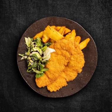 Kızarmış tavuk göğsü filetosu ve koyu arkaplanda patates dilimleri.