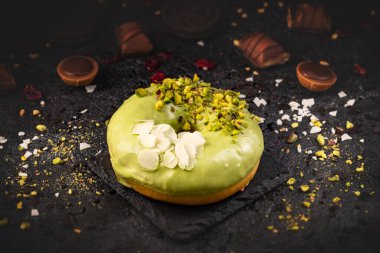 Yeşil jöleli donut, şam fıstıklı ve badem taneli siyah kaplama arka planda.