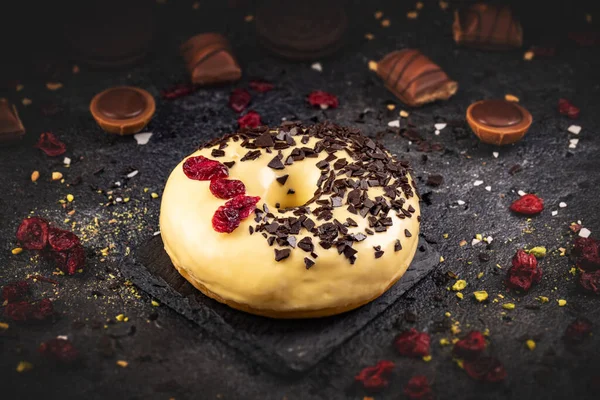 Donut Geel Glazuur Met Chocoladevlokken Gedroogde Veenbessen Zwarte Leisteenachtergrond — Stockfoto