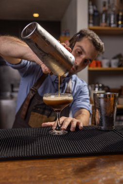 Barmen dikkatli bir şekilde içkiden espresso martinisini barın üstünde bir coupe bardağına dolduruyor.