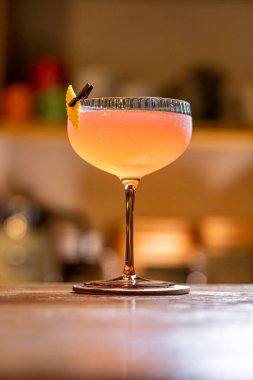 Pembe kokteyl, ahşap tezgahta portakal kabuğuyla servis edilir.