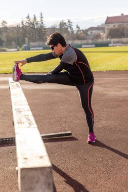 Stadyumdaki engelli koşuda bacağını esneten atlet kadın.