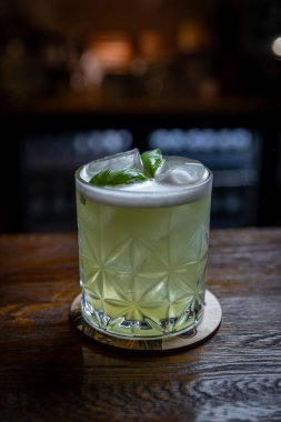 Kırsal ahşap tezgahta buzlu ve köpüklü yeşil fesleğen kokteyli.