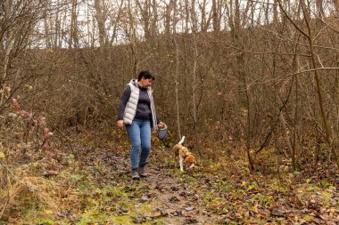 Kadın ve av köpeği sonbahar ormanlarında çamurlu bir yolda yürüyorlar.