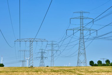 Arka planda rüzgar türbinleri olan elektrik direkleri ve elektrik hatları